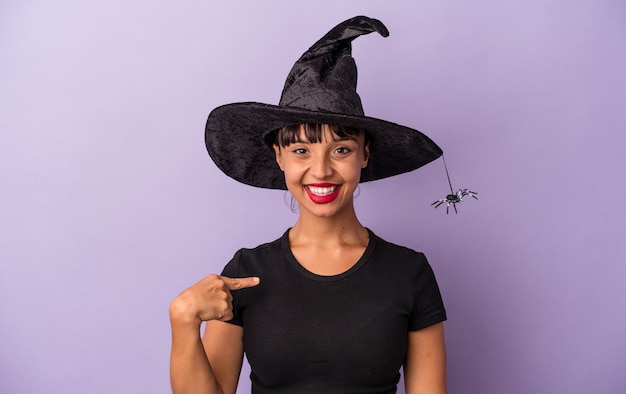 Jeune femme métisse déguisée en sorcière isolée sur fond violet personne pointant à la main vers un espace de copie de chemise, fière et confiante
