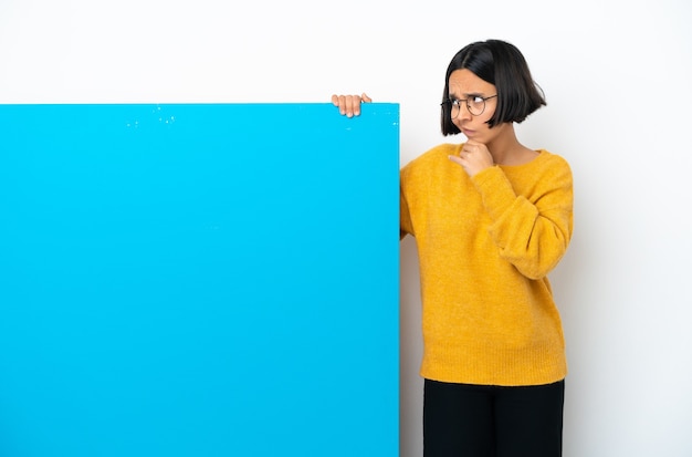 Jeune femme métisse avec une grande pancarte bleue isolée sur fond blanc ayant des doutes et avec une expression de visage confuse