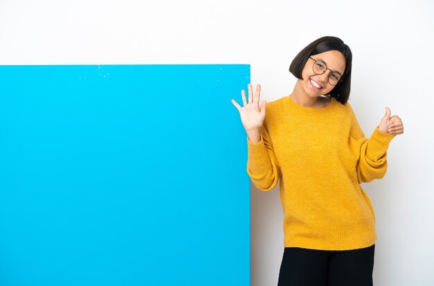 Jeune femme métisse avec une grande pancarte bleue isolée sur fond blanc en comptant six avec les doigts