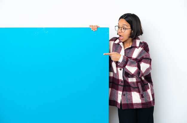 Jeune femme métisse avec une grande pancarte bleue isolée sur fond blanc pointant vers l'extérieur