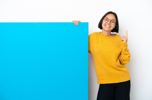 Jeune femme métisse avec une grande pancarte bleue isolée sur fond blanc pointant vers le haut une excellente idée