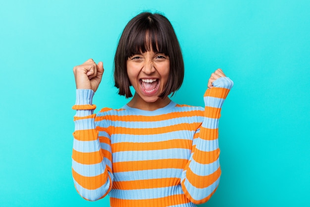 Jeune femme métisse isolée sur fond bleu célébrant une victoire, une passion et un enthousiasme, une expression heureuse.