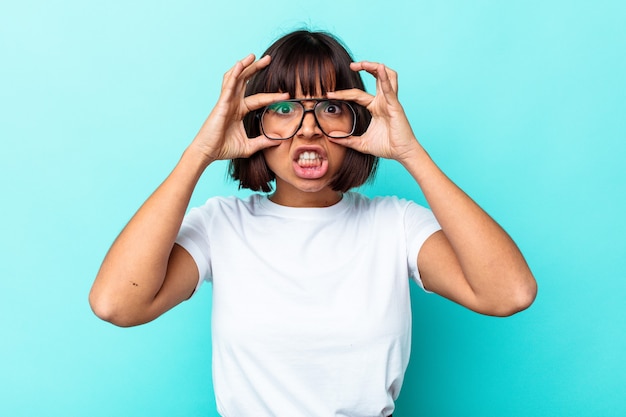 Jeune femme métisse isolée sur fond bleu en gardant les yeux ouverts pour trouver une opportunité de réussite.