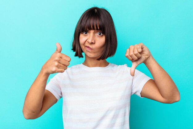 Jeune femme métisse isolée sur fond bleu montrant les pouces vers le haut et les pouces vers le bas, concept difficile à choisir