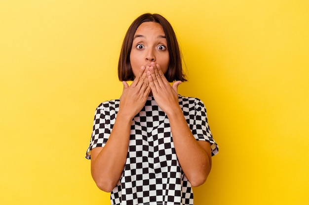 Jeune femme métisse isolée sur fond jaune choquée couvrant la bouche avec les mains.