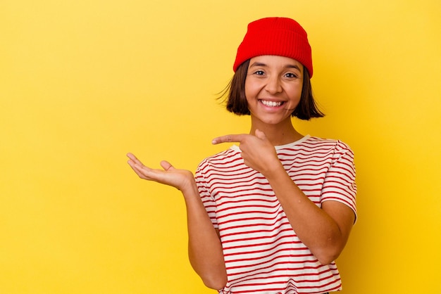 Jeune femme métisse isolée sur fond jaune excitée tenant un espace de copie sur la paume.