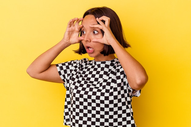 Jeune femme métisse isolée sur fond jaune en gardant les yeux ouverts pour trouver une opportunité de réussite.