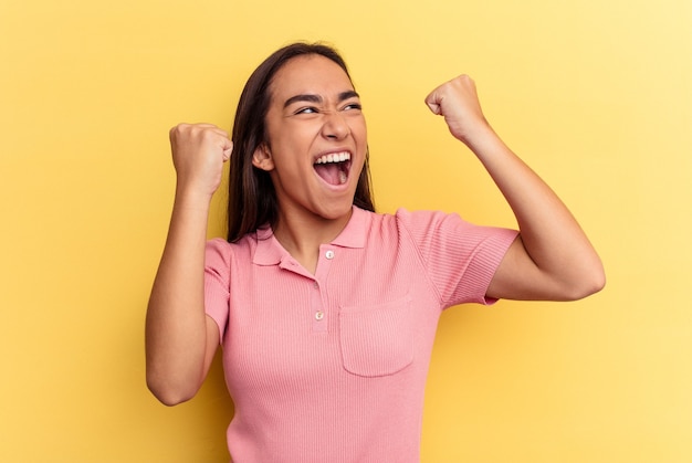 Jeune femme métisse isolée sur fond jaune levant le poing après une victoire, concept gagnant.