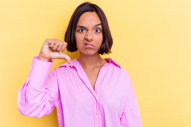 Jeune femme métisse isolée sur fond jaune montrant un geste d'aversion, les pouces vers le bas. Concept de désaccord.