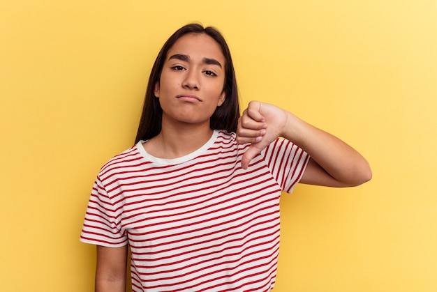 Jeune femme métisse isolée sur fond jaune montrant un geste d'aversion, les pouces vers le bas. Notion de désaccord.