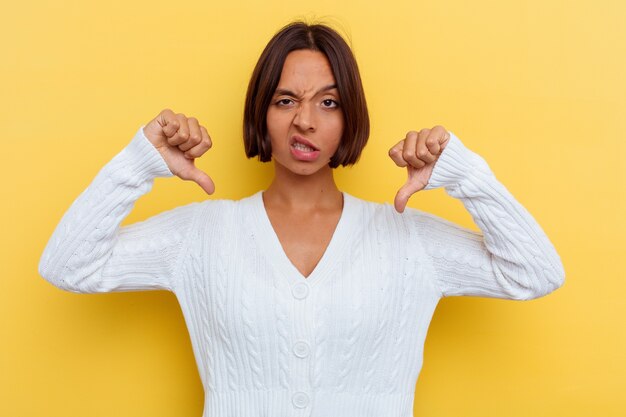 Jeune femme métisse isolée sur fond jaune montrant le pouce vers le bas et exprimant son aversion.