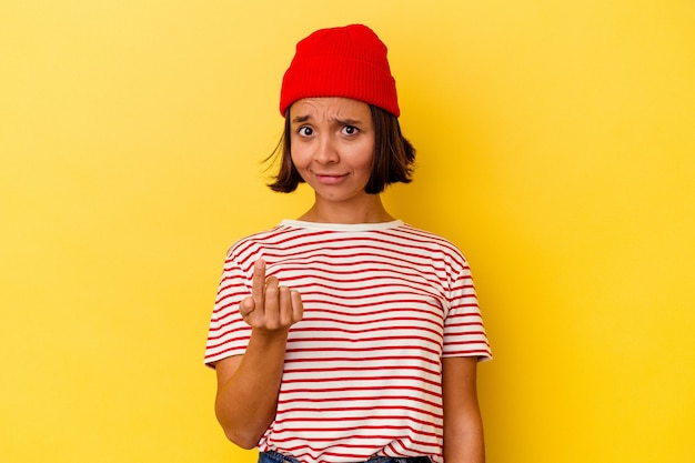 Jeune femme métisse isolée sur fond jaune pointant du doigt vers vous comme si vous vous invitiez à vous rapprocher.