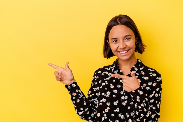 Jeune femme métisse isolée sur fond jaune pointant avec les index vers un espace de copie, exprimant l'excitation et le désir.