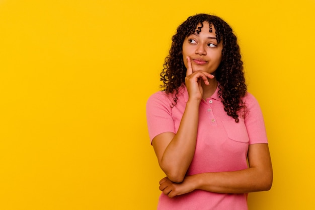 Jeune femme métisse isolée sur fond jaune à la recherche de côté avec une expression douteuse et sceptique.