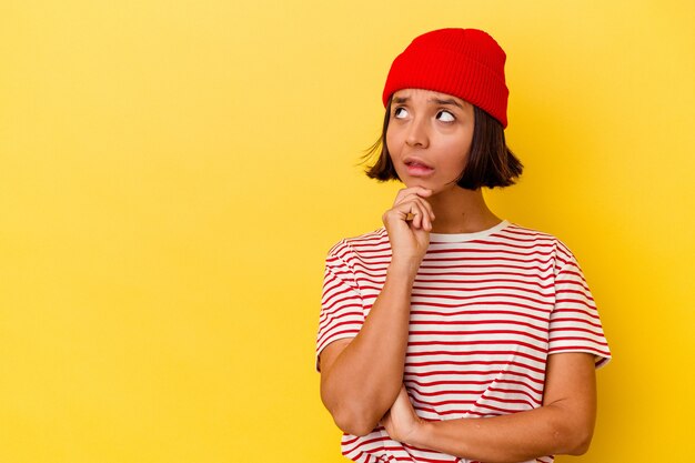 Jeune femme métisse isolée sur fond jaune regardant de côté avec une expression douteuse et sceptique.