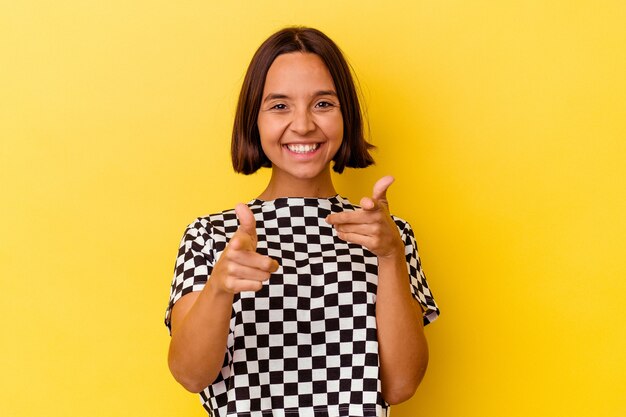 Jeune femme métisse isolée sur fond jaune sourires joyeux pointant vers l'avant.