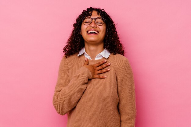 Jeune femme métisse isolée sur fond rose éclate de rire en gardant la main sur la poitrine.