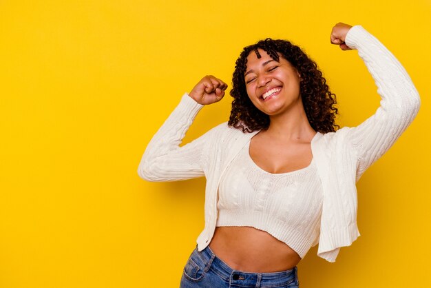 Jeune femme métisse isolée sur mur jaune levant le poing après une victoire, concept gagnant.