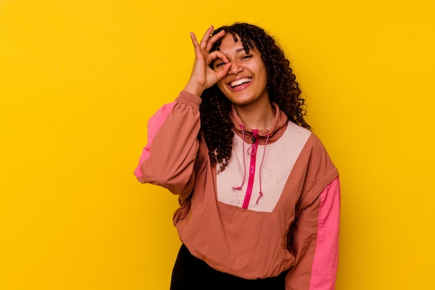 Jeune femme métisse isolée sur un mur rose excité en gardant le geste ok sur les yeux.