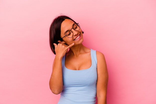 Jeune femme métisse isolée sur un mur rose montrant un geste d'appel de téléphone mobile avec les doigts.