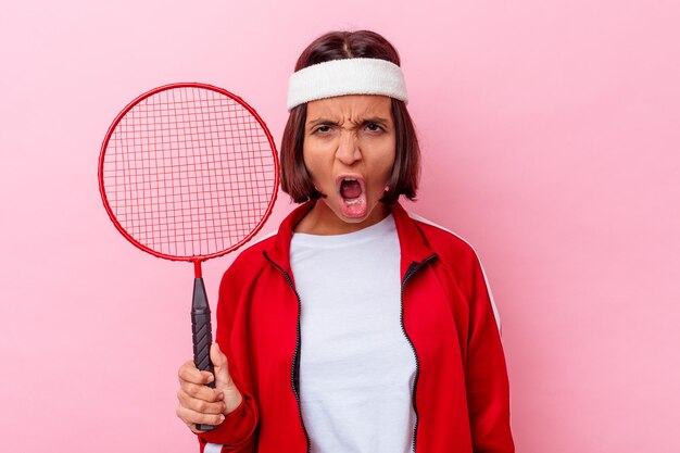 Jeune femme métisse jouant au badminton isolé sur un mur rose criant très en colère et agressif.