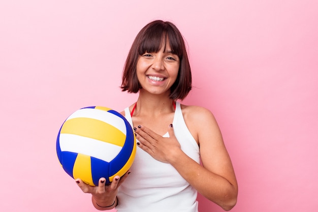 Jeune femme métisse jouant au volley-ball isolée sur fond rose rit fort en gardant la main sur la poitrine.