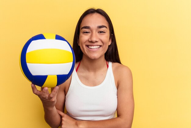 Jeune femme métisse jouant au volley-ball sur la plage isolée sur fond jaune en riant et en s'amusant.