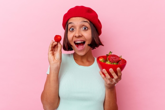 Jeune femme métisse mangeant des fraises isolé sur un mur rose