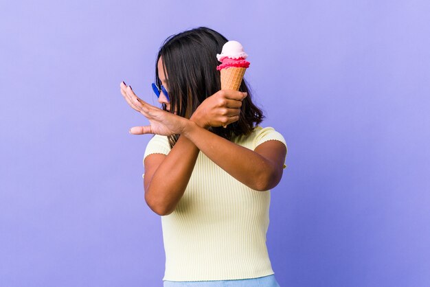 Jeune femme métisse mangeant une glace en gardant les deux bras croisés, concept de déni.