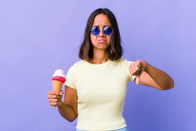 Jeune femme métisse mangeant une glace montrant les pouces vers le haut et les pouces vers le bas, concept difficile à choisir