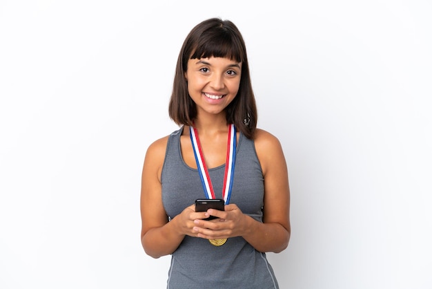 Jeune femme métisse avec des médailles isolées sur fond blanc envoyant un message avec le mobile