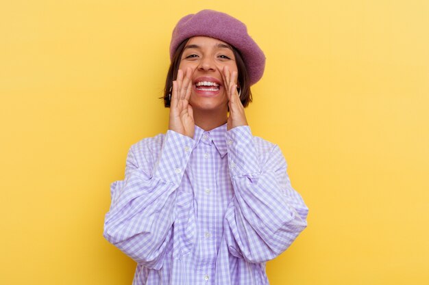 Jeune femme métisse portant un béret isolé sur fond jaune criant excité à l'avant.