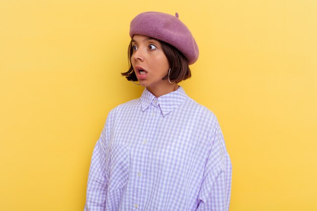 Jeune femme métisse portant un béret isolé sur fond jaune étant choquée à cause de quelque chose qu'elle a vu.