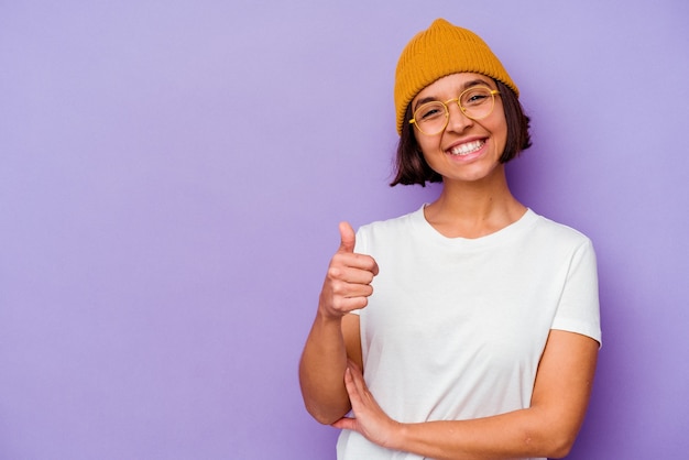 Jeune femme métisse portant un bonnet de laine isolé sur fond violet souriant et levant le pouce vers le haut