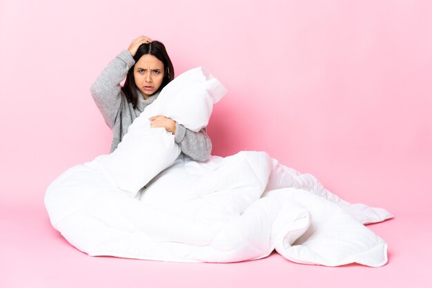 Jeune femme métisse portant pijama assis sur le sol avec une expression de frustration et de ne pas comprendre