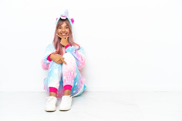 Jeune femme métisse portant un pyjama licorne assis sur le sol isolé sur fond blanc souriant