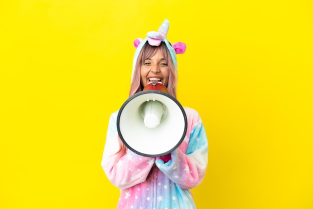 Jeune femme métisse portant un pyjama licorne isolé sur fond blanc criant à travers un mégaphone