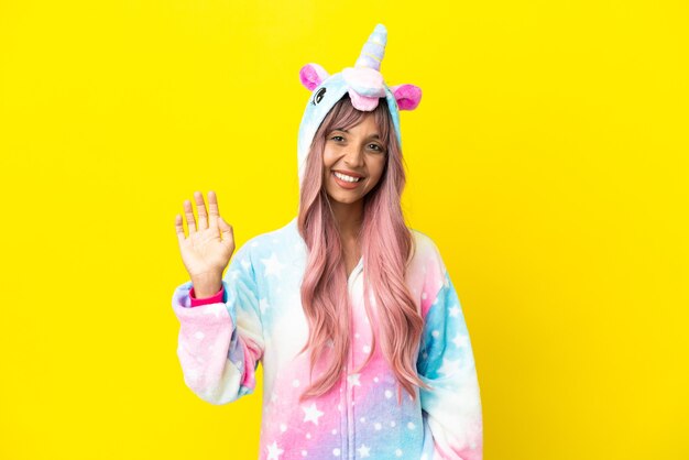 Jeune femme métisse portant un pyjama licorne isolé sur fond blanc saluant avec la main avec une expression heureuse