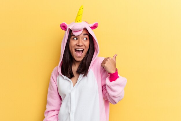 Jeune femme métisse portant un pyjama de licorne isolé sur des points de fond jaune avec le pouce loin, riant et insouciant.