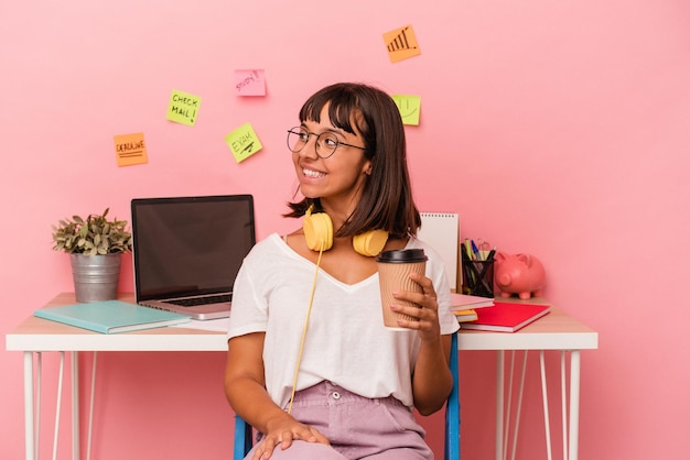 Jeune femme métisse préparant un examen dans la salle tenant un café isolé sur fond rose regarde de côté souriant gai et agréable