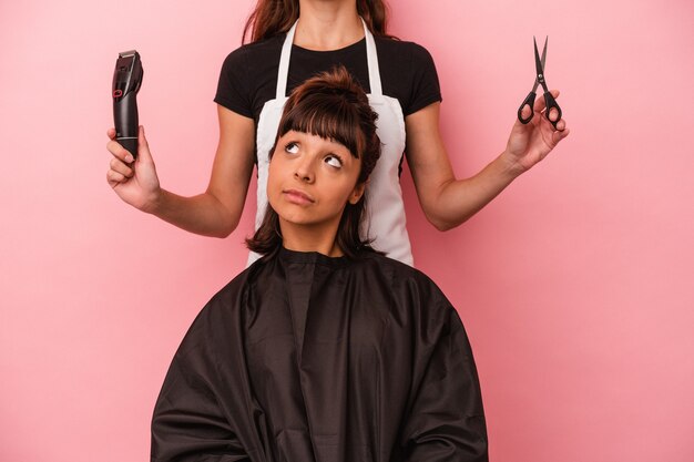 Jeune femme métisse se faisant couper les cheveux chez le coiffeur isolé sur fond rose rêvant d'atteindre ses objectifs