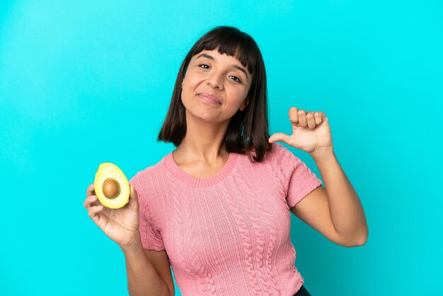 Jeune femme métisse tenant un avocat isolé sur fond bleu fier et satisfait de soi