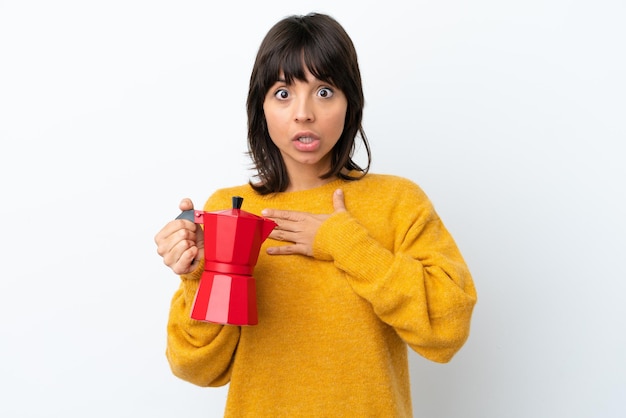 Jeune femme métisse tenant une cafetière isolée sur fond blanc surprise et choquée en regardant à droite