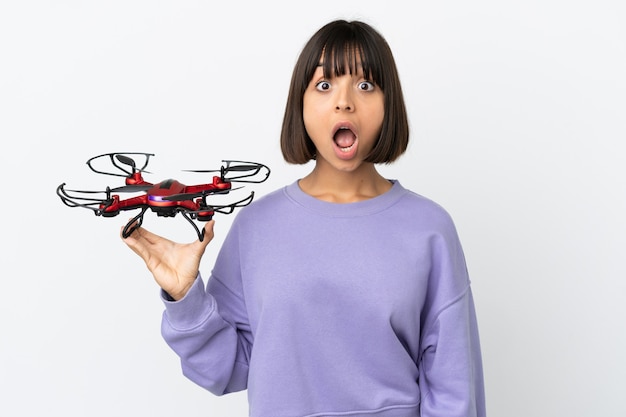 Jeune femme métisse tenant un drone isolé sur fond blanc avec une expression faciale surprise