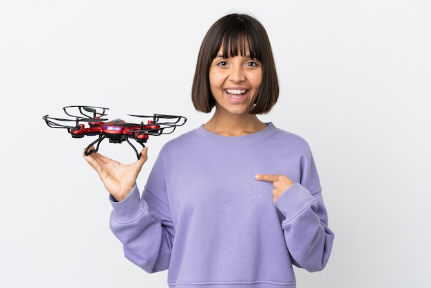 Jeune femme métisse tenant un drone isolé sur fond blanc avec une expression faciale surprise