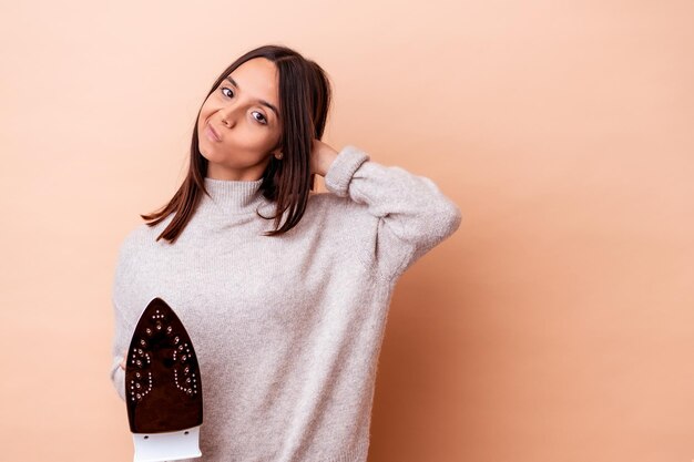 Jeune femme métisse tenant un fer isolé touchant l'arrière de la tête, en pensant et en faisant un choix.