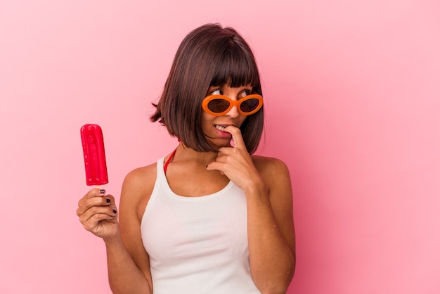 Jeune femme métisse tenant une glace isolée sur fond bleu détendue en pensant à quelque chose en regardant un espace de copie.