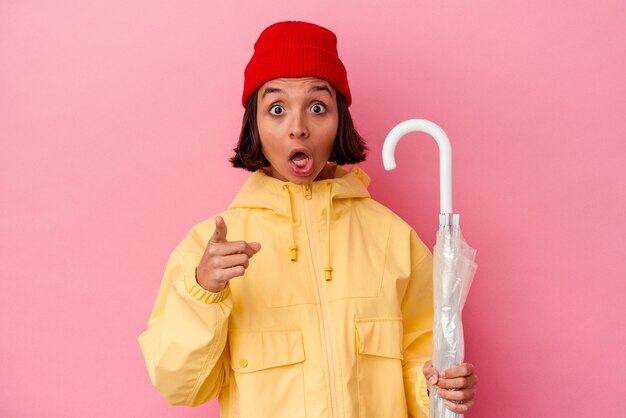 Jeune femme métisse tenant un parapluie isolé sur fond rose ayant une idée, un concept d'inspiration.