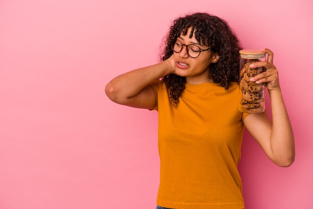 Jeune femme métisse tenant un pot de biscuits isolé sur fond rose touchant l'arrière de la tête, pensant et faisant un choix.