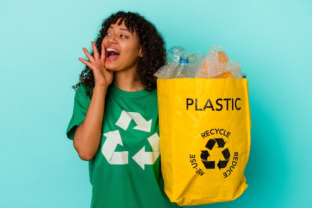 Jeune femme métisse tenant un sac en plastique recyclé isolé sur fond bleu criant et tenant la paume près de la bouche ouverte.